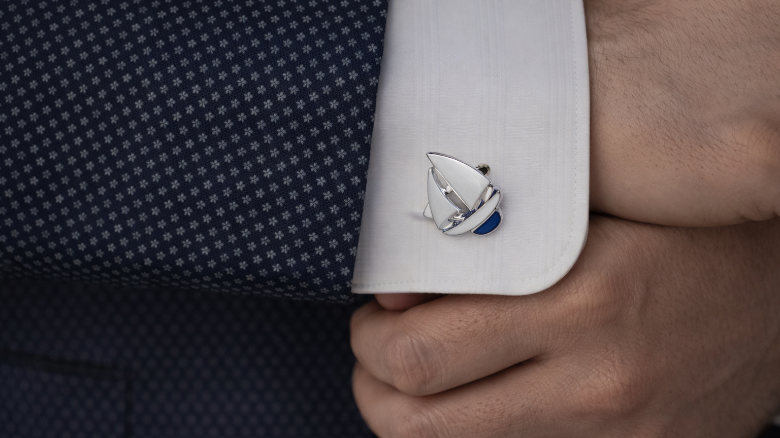Cufflink with a sailboat design on a white cuff against a dark suit background