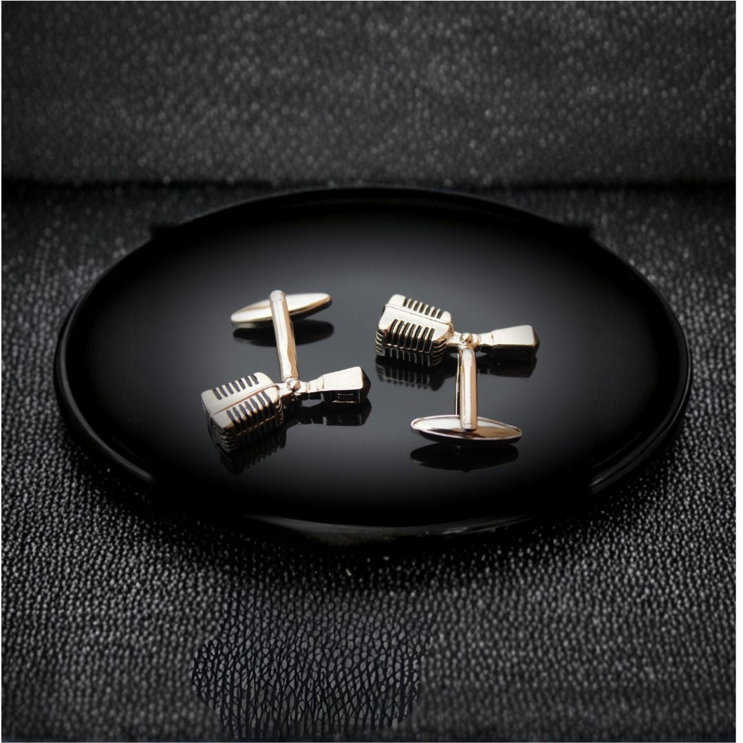 Microphone-shaped cufflinks on a black plate with a dark textured background