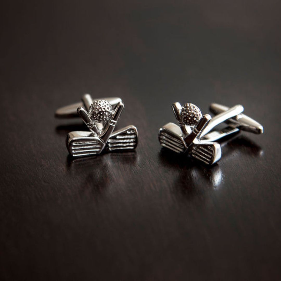 Silver golf clubs and ball cufflinks on a dark surface