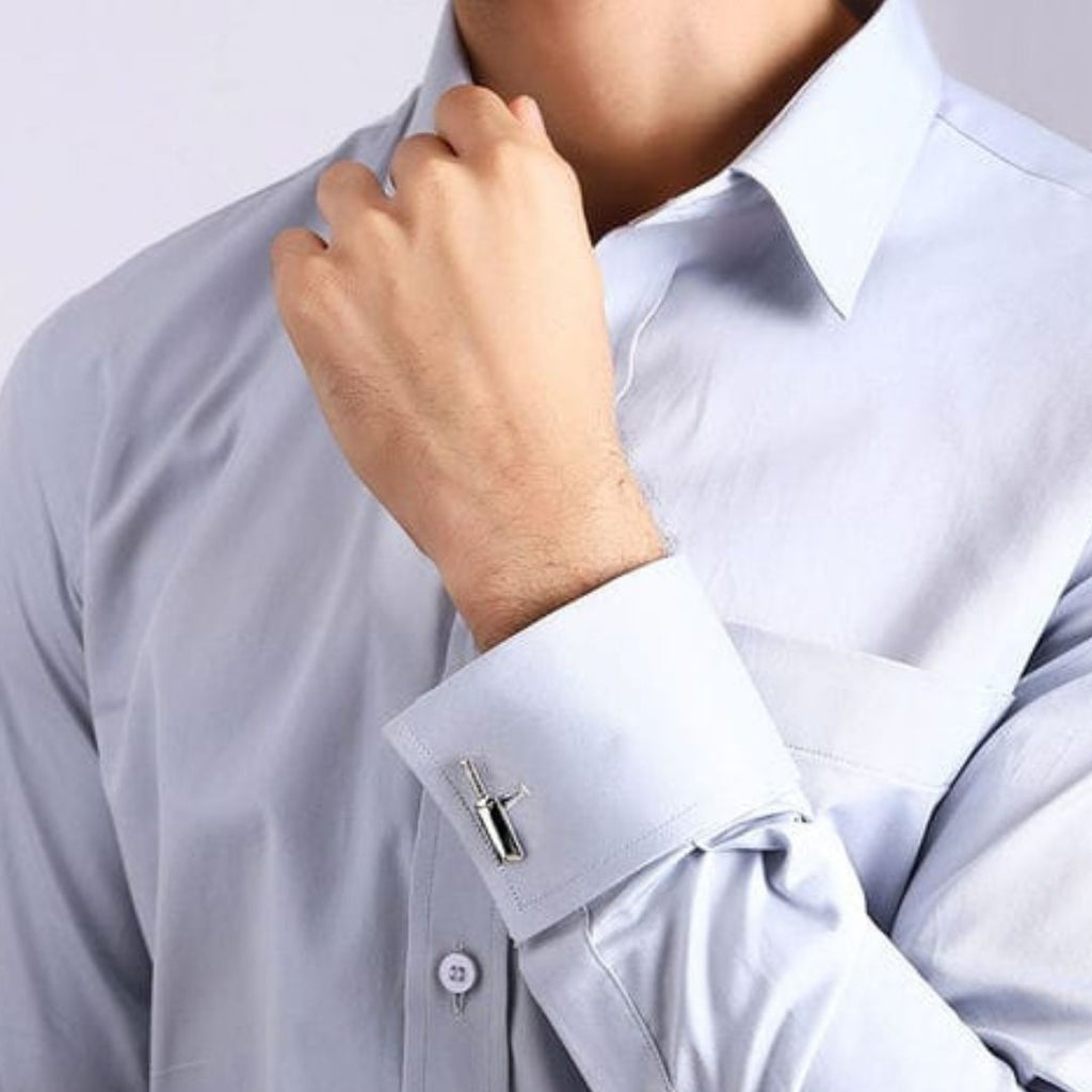 Close-up of a person adjusting the cuff of a light grey dress shirt with a cricket bat cufflink