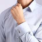Close-up of a person adjusting the cuff of a light grey dress shirt with a cricket bat cufflink